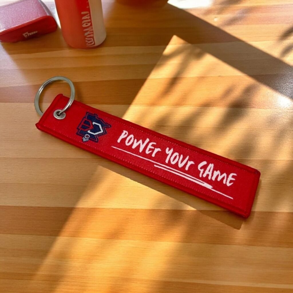 Czerwony brelok materiałowy z białym haftem logo w stylu Remove Before Flight.